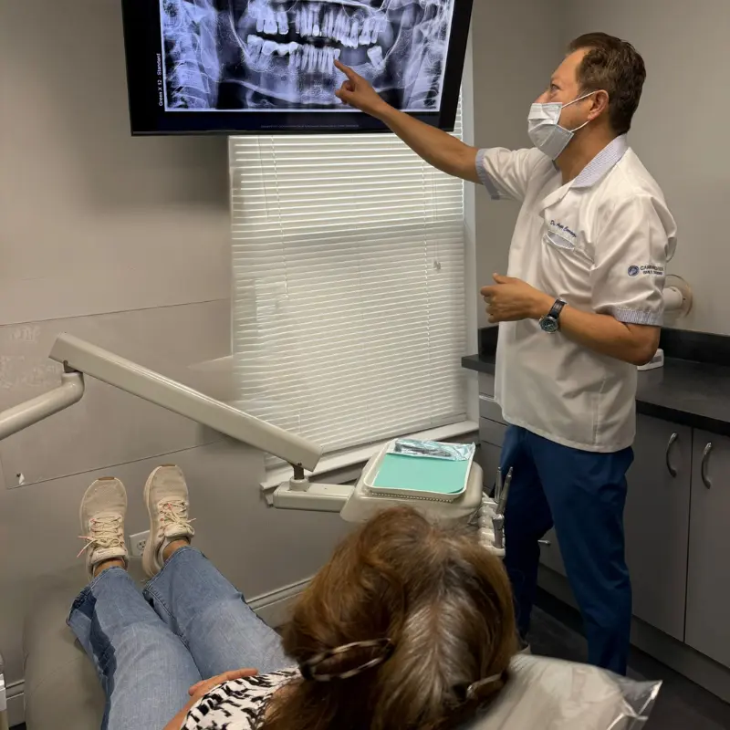 Dr. Aristo Carranza explaining a patient's panoramic dental x-ray on a large screen during a comprehensive consultation at Smile Design NJ.